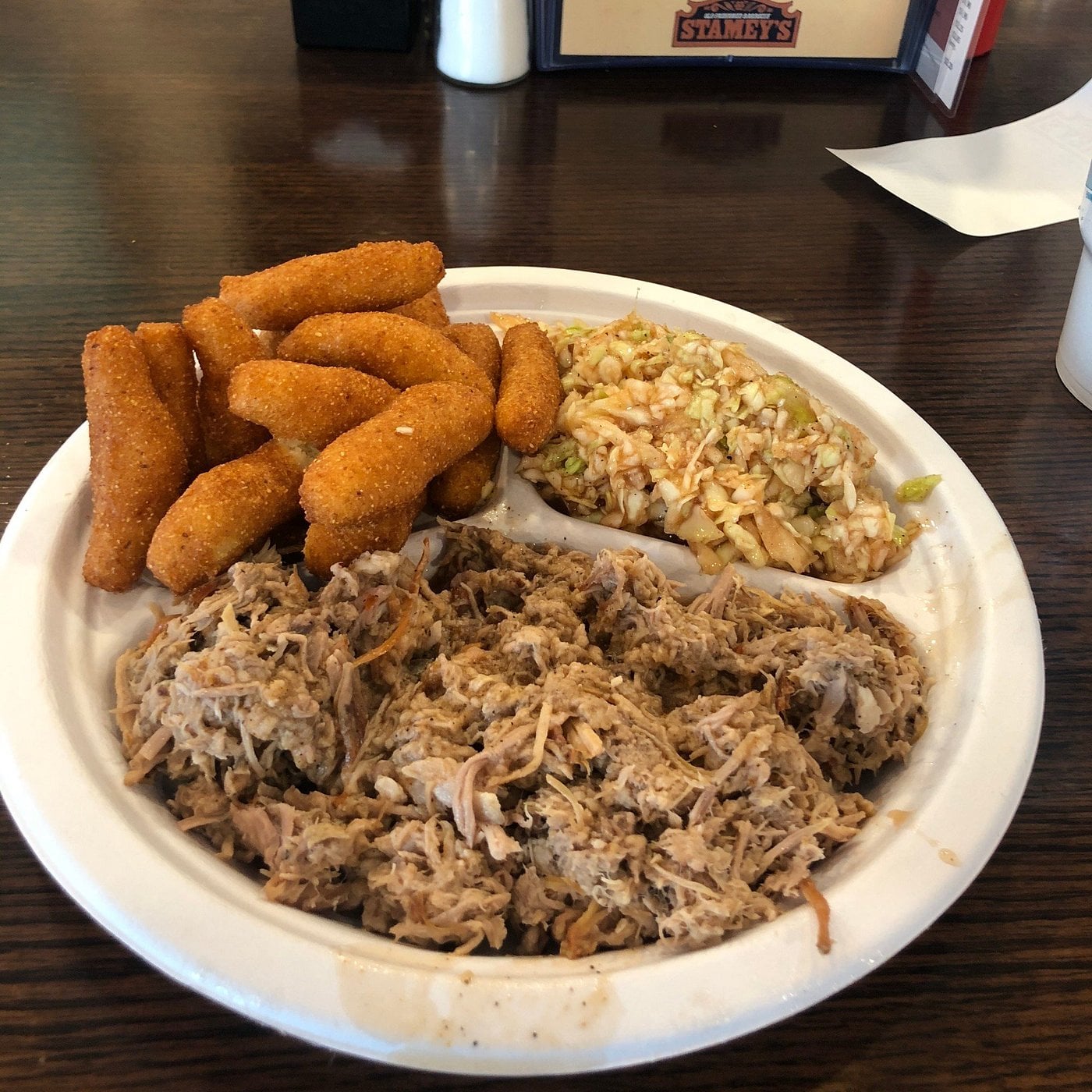 A plate with pulled pork, fried mozzarella sticks, and a serving of coleslaw on a dark wooden table.