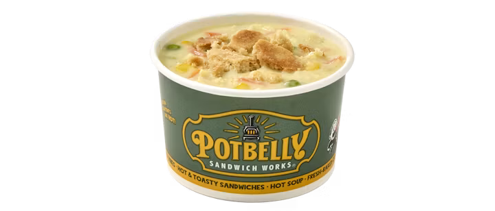 A green Potbelly Sandwich Works cup filled with creamy soup, showing chunks of vegetables and topped with crushed crackers.