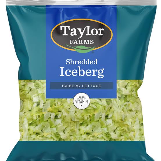 A bag of Taylor Farms Shredded Iceberg Lettuce, featuring green shredded lettuce inside a blue and clear package labeled with the brand, product name, and a note about Vitamin K.