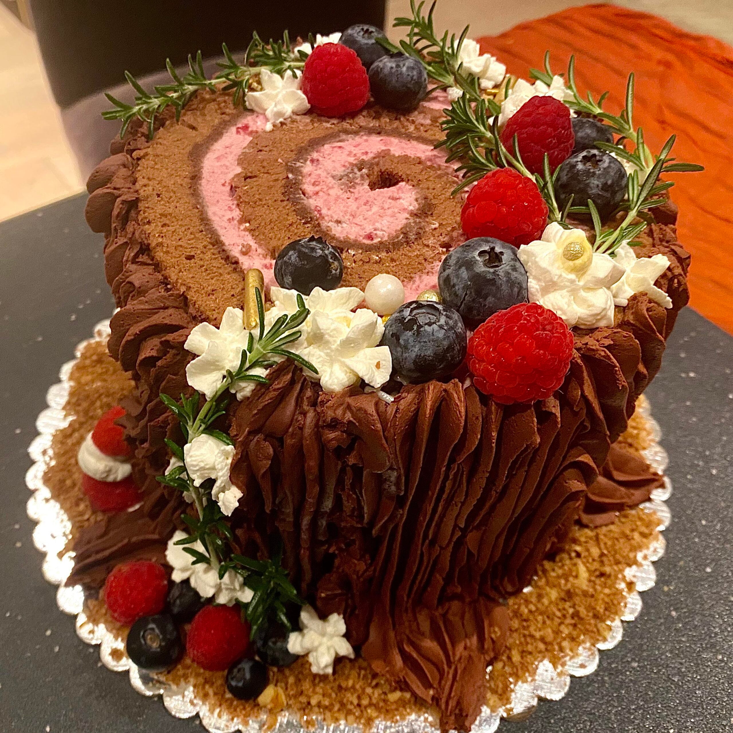 This chocolate cake, styled like a tree stump, is one of those charming homemade Christmas treats—topped with whipped cream, blueberries, raspberries, rosemary sprigs, and small mushrooms. Presented on a golden tray with crushed cookie “soil,” it brings festive woodland magic to your holiday table.