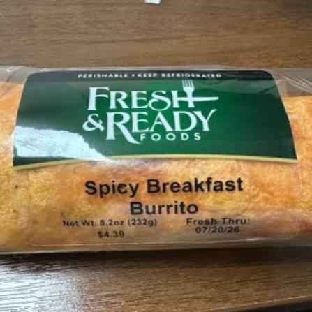 A packaged Fresh & Ready Foods Spicy Breakfast Burrito sits on a wooden surface. The label shows the price, net weight, and expiration date.