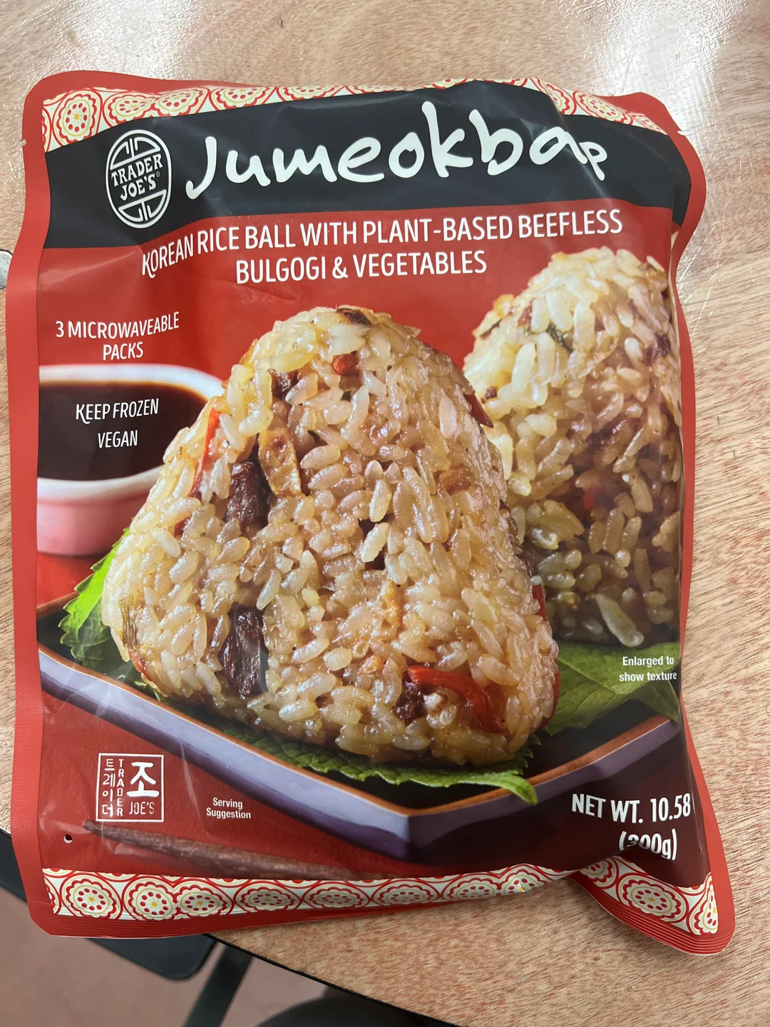 A red package of Trader Joe’s Jumeokbap, Korean rice balls with plant-based beefless bulgogi and vegetables, sits on a wooden surface. The package shows an image of the rice ball.