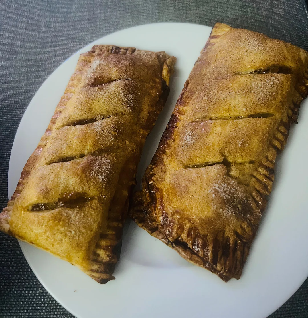 Two rectangular pastries with golden brown crusts and sugar on top, placed side by side on a white plate with a dark textured background.