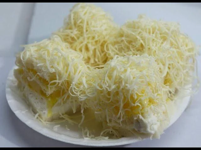 Four pieces of cake topped with grated cheese are arranged on a white plate. The cakes have a creamy filling and appear to be moist and rich, with cheese generously sprinkled on top.