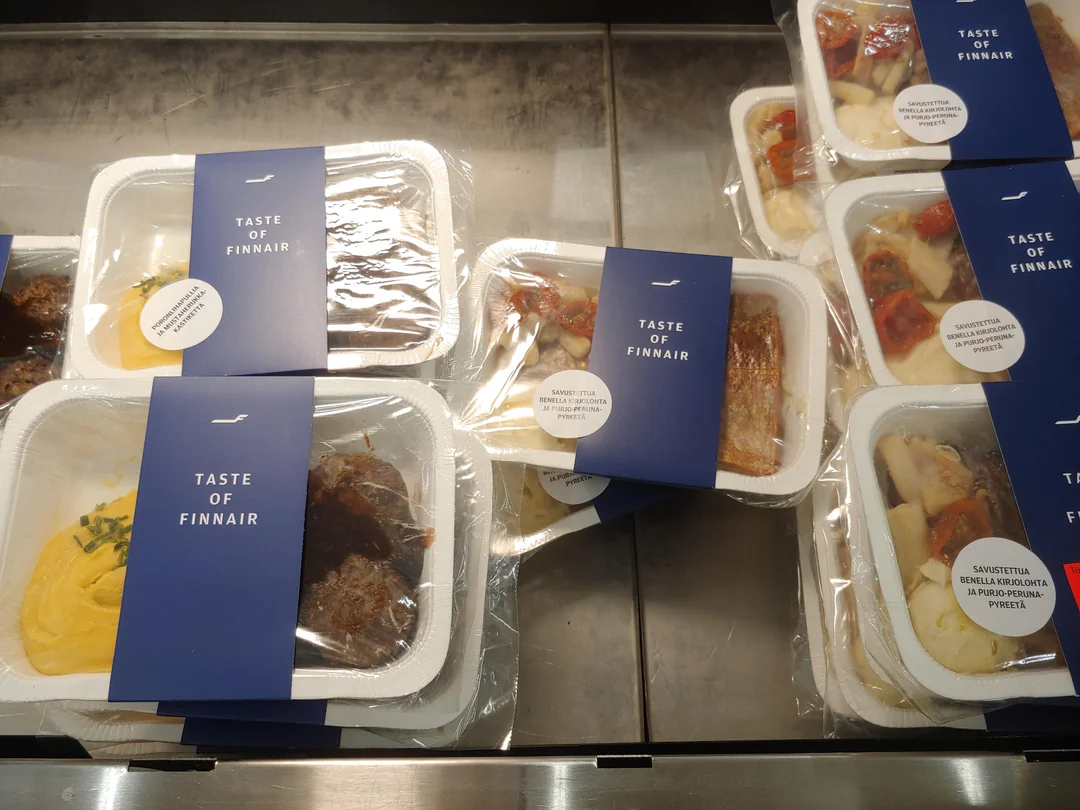 Pre-packaged airline meals labeled “Taste of Finnair” are stacked in a display case. The meals are sealed in plastic trays, each with a blue card and visible contents such as potatoes, meat, and vegetables.