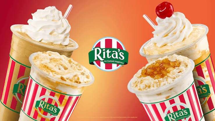 Four Rita’s frozen drinks with whipped cream, a cherry, and caramel topping are displayed against a red-orange gradient background. The Rita’s logo is centered in the middle.