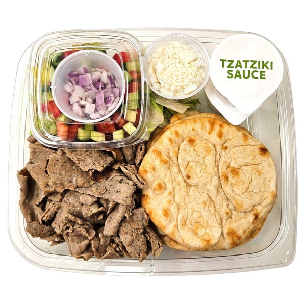 Plastic tray with sliced gyro meat, two pita breads, a cup of chopped salad, feta cheese, and a container labeled “Tzatziki Sauce,” arranged neatly for a meal.