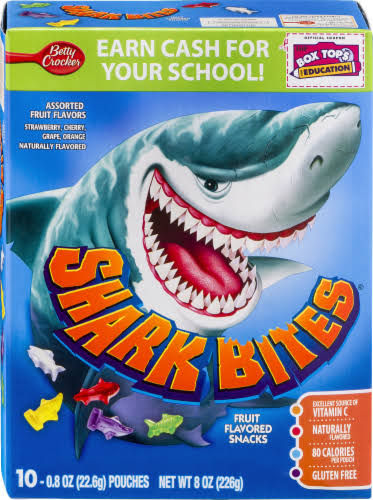 A colorful box of Shark Bites fruit snacks featuring a cartoon shark with an open mouth, bold “Shark Bites” text, and information about flavors and nutrition. Box shows 10 pouches and a “Box Tops for Education” label.