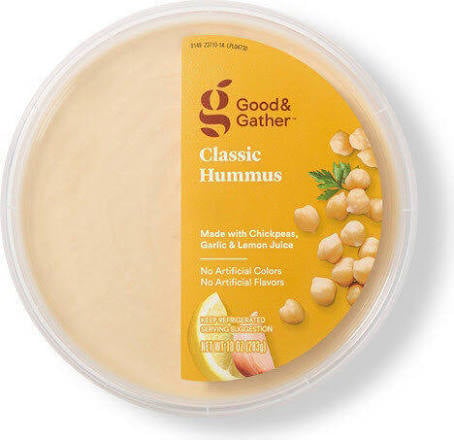 A round container of Good & Gather Classic Hummus with a yellow label showing chickpeas, garlic, lemon, and parsley. The label highlights that it’s made with chickpeas, garlic, lemon juice, and has no artificial colors.