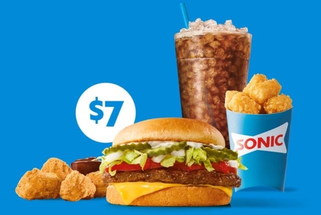 A cheeseburger with lettuce, tomato, and pickles, golden tater tots, chicken nuggets, a cup of sauce, and a large soda on a blue background with a “$7” sign and a Sonic logo on the fries container.