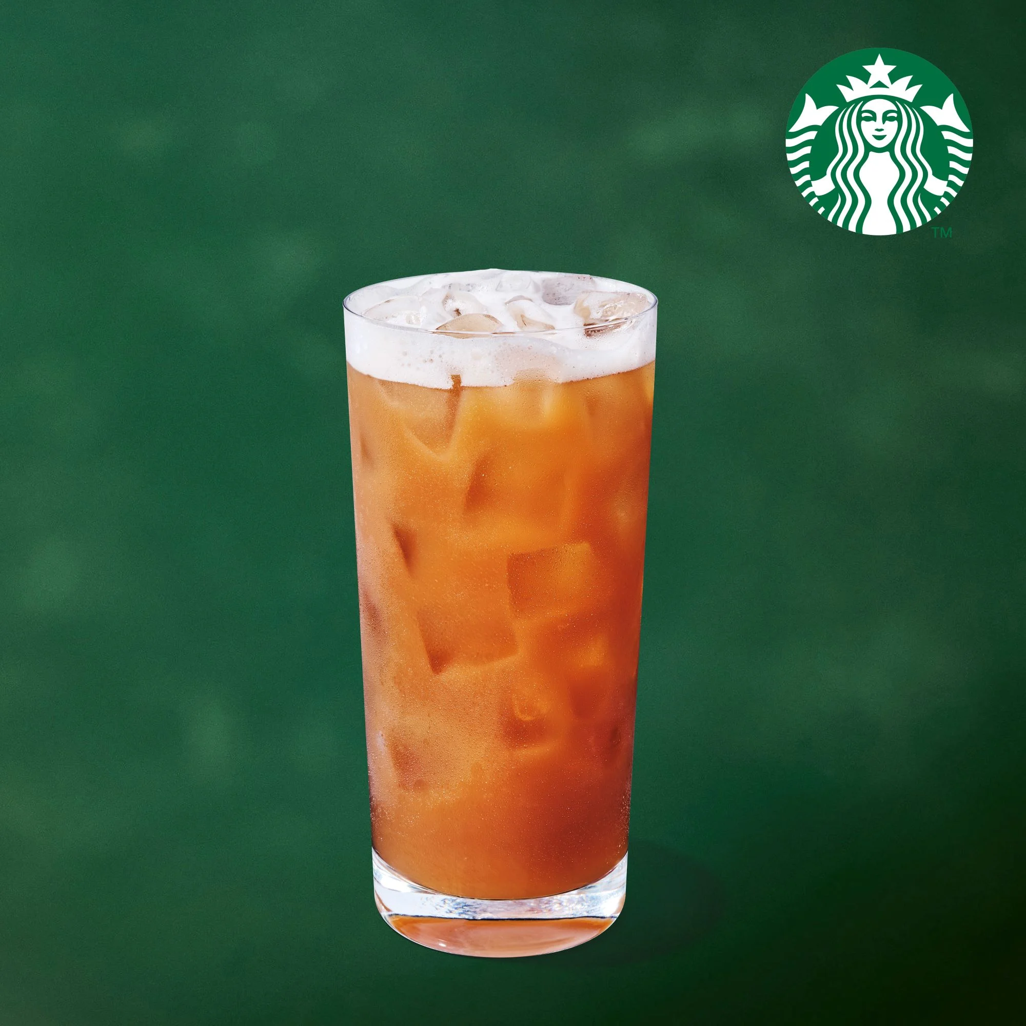 A tall glass of iced tea with a foamy top is filled with ice, set against a green background with the Starbucks logo in the upper right corner.