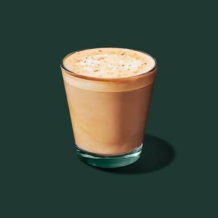 A glass of frothy coffee with a creamy layer on top, set against a dark green background.
