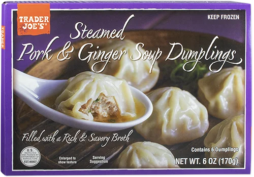 Box of Trader Joe’s Steamed Pork & Ginger Soup Dumplings, showing dumplings on a plate with one cut open to reveal the filling. Text highlights six dumplings filled with pork, ginger, and savory broth.