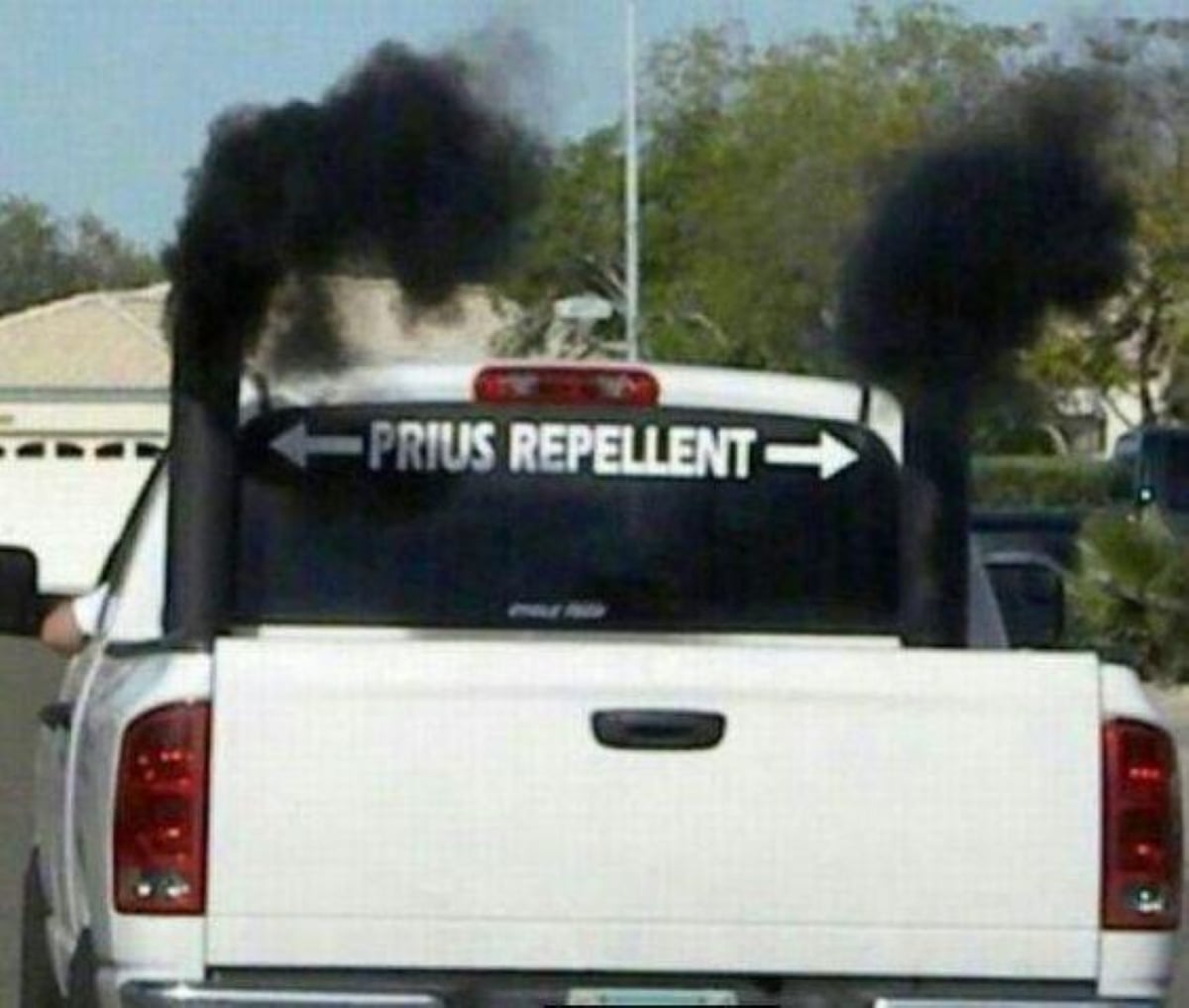 A white pickup truck emits black smoke from two large exhaust pipes, with a rear window sticker reading “PRIUS REPELLENT” and arrows pointing to the smoke.