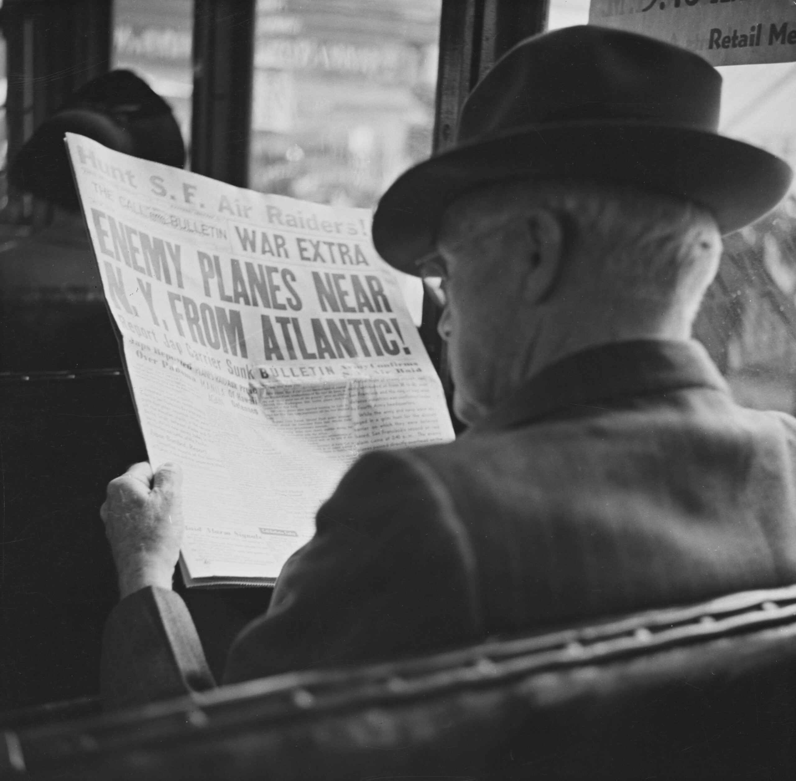 An older man in a hat reads a newspaper on a bus. The headline warns, “ENEMY PLANES NEAR N.Y. FROM ATLANTIC!” The scene appears to be from the World War II era.