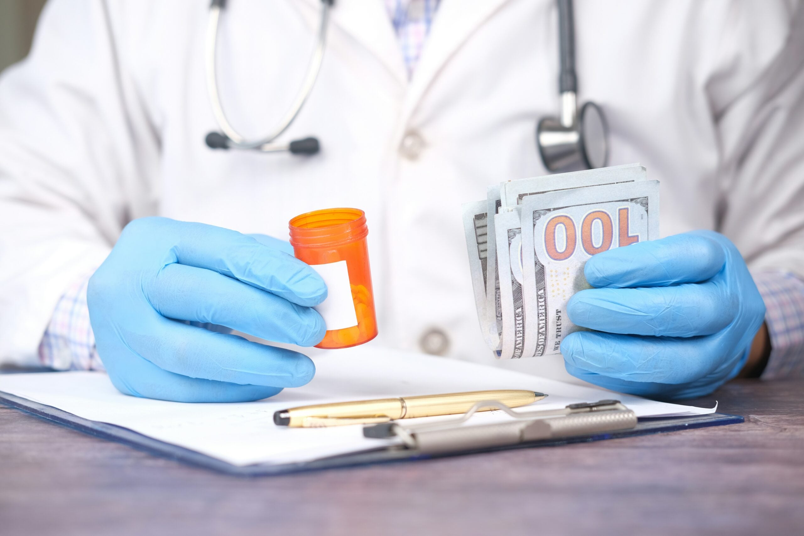 A doctor in a white coat and blue gloves holds a pill bottle in one hand and a stack of hundred-dollar bills in the other, with a clipboard, pen, and stethoscope visible on the table—offering a thought-provoking glimpse into the realities of healthcare and financial decisions that may shape life in 2026.