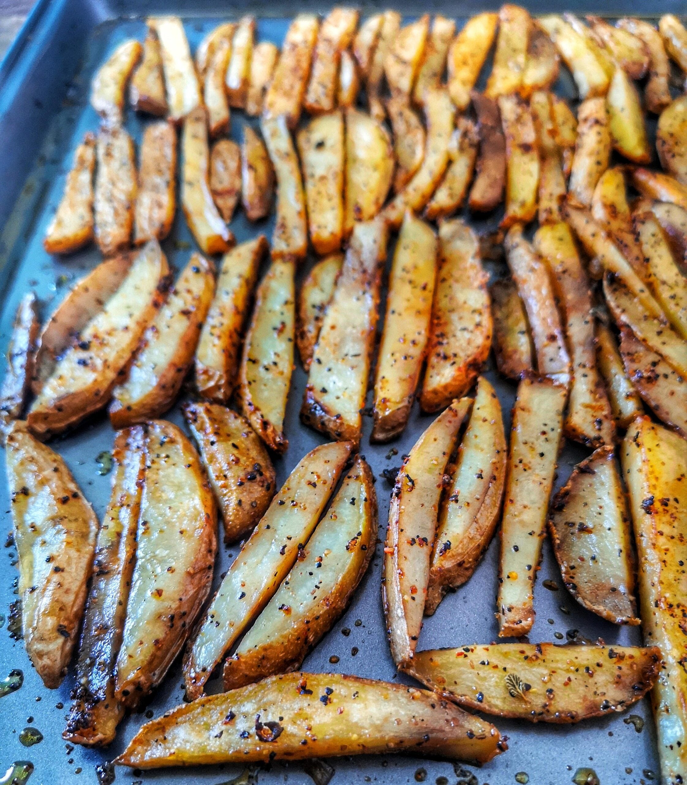 A baking tray filled with golden-brown potato wedges, seasoned with spices, arranged neatly in rows, fresh out of the oven.