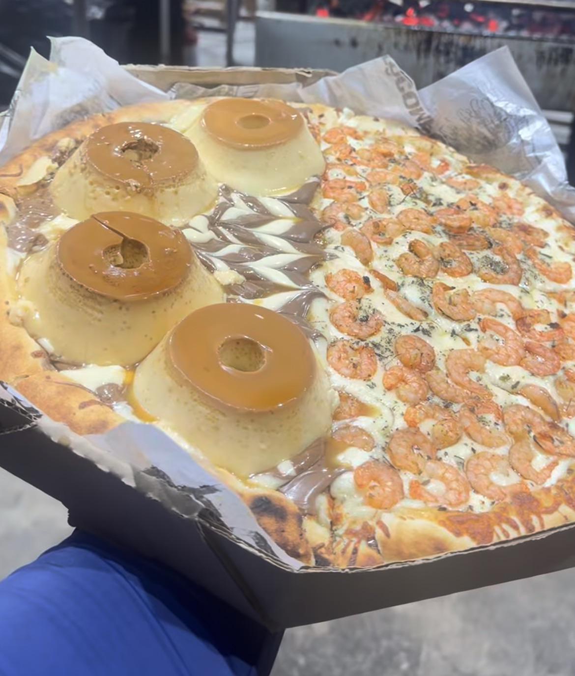A pizza divided in half: one side topped with caramel flan and chocolate spread, the other with melted cheese and shrimp, held in a cardboard tray.