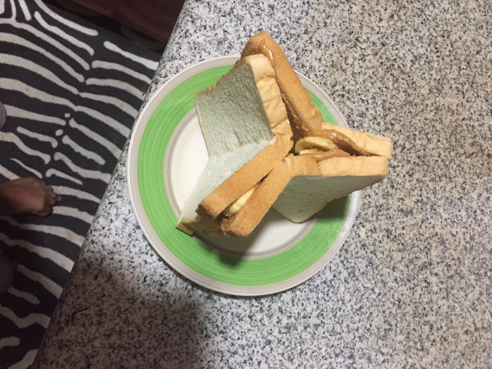 A sandwich with peanut butter and banana slices sits on a small green and white plate, placed on a granite countertop next to a black and white zebra-print rug.