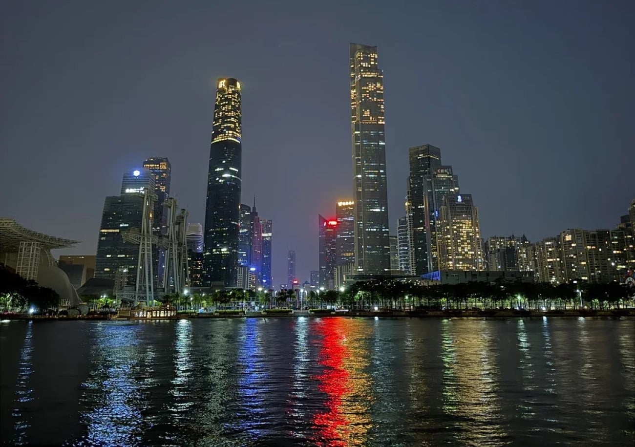 A city skyline at night with tall, illuminated skyscrapers reflected in the calm water below—a breathtaking scene reminiscent of the Biggest Cities In The World. The sky is dark, and various building lights create colorful reflections on the surface.