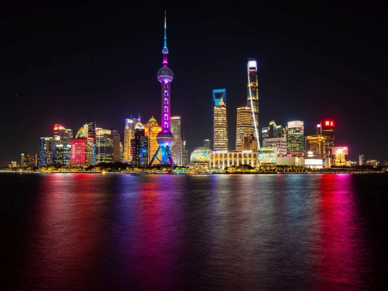 Beijing skyline at night with brightly lit skyscrapers, including the iconic Oriental Pearl Tower, reflected in the water below—a breathtaking view of one of the Biggest Cities In The World.