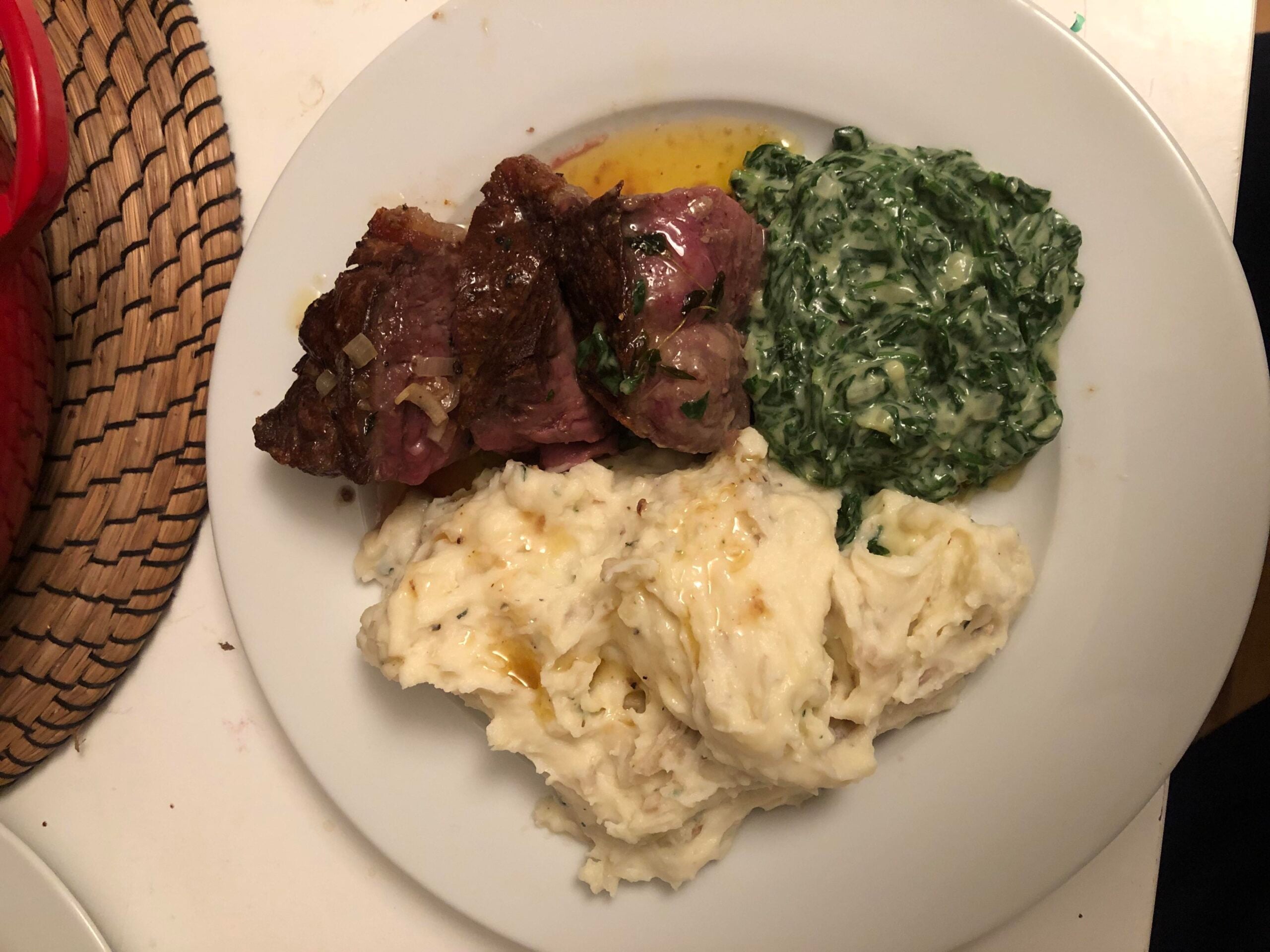 A white plate with slices of cooked steak, creamy mashed potatoes, and a serving of creamed spinach.