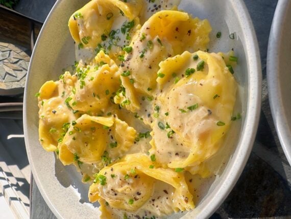 A plate of large ravioli covered in a creamy sauce, garnished with chopped chives and freshly ground black pepper, served in a shallow dish&mdash;perfect for anyone who loves beautiful photos of pasta.