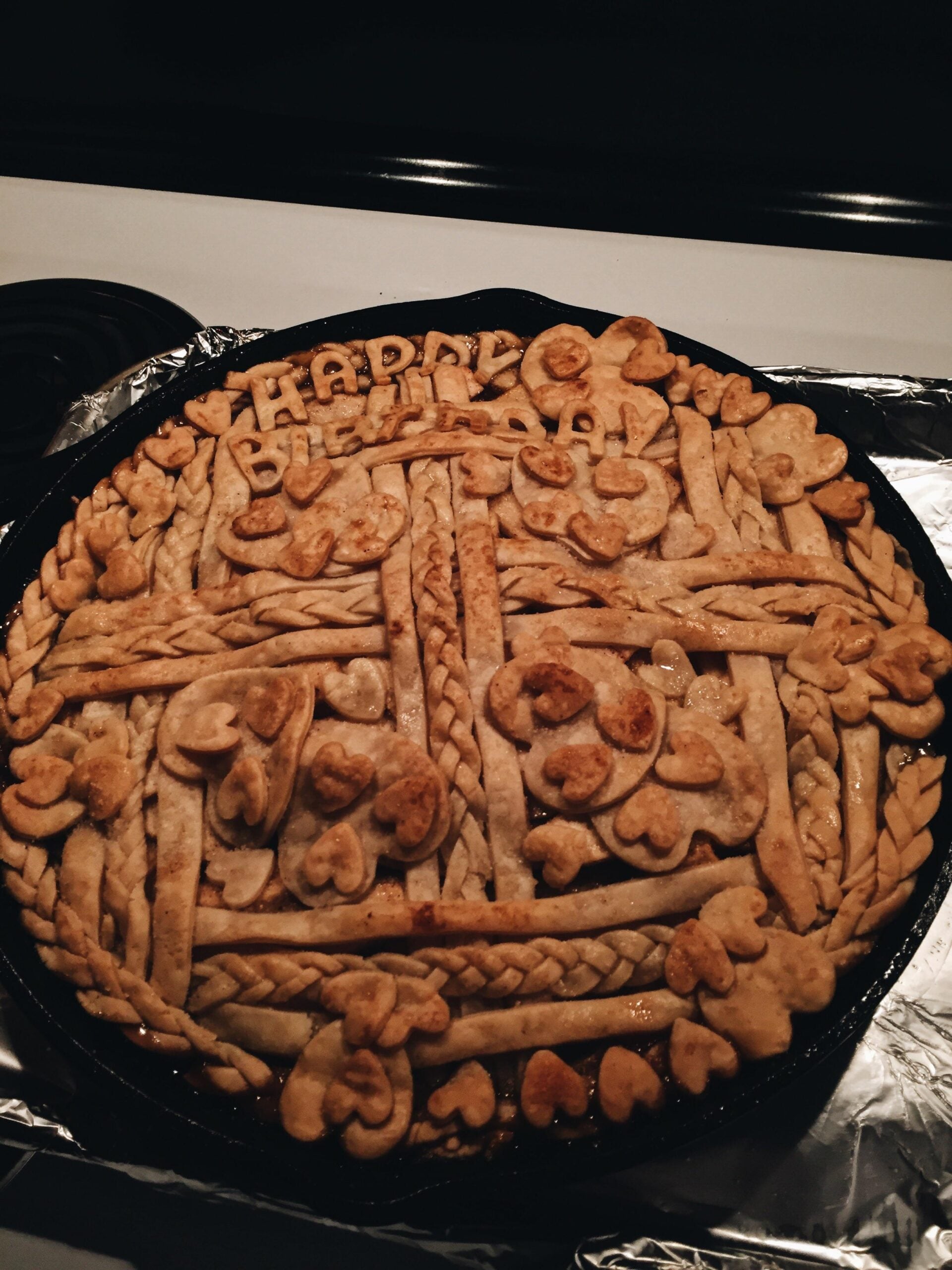 A pie with intricate lattice and braided crust, decorated with small heart shapes and the words “Happy Birthday” spelled out in dough on top.