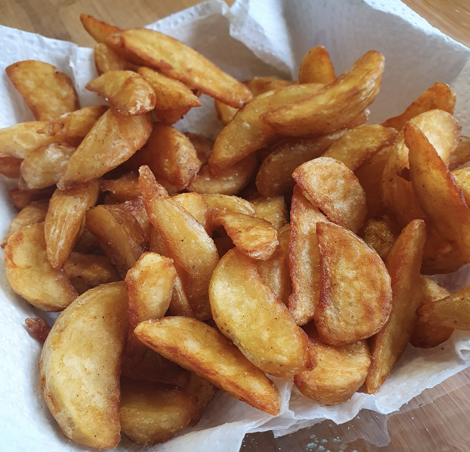 A close-up of golden, crispy potato wedges on a white paper towel, served in a bowl.