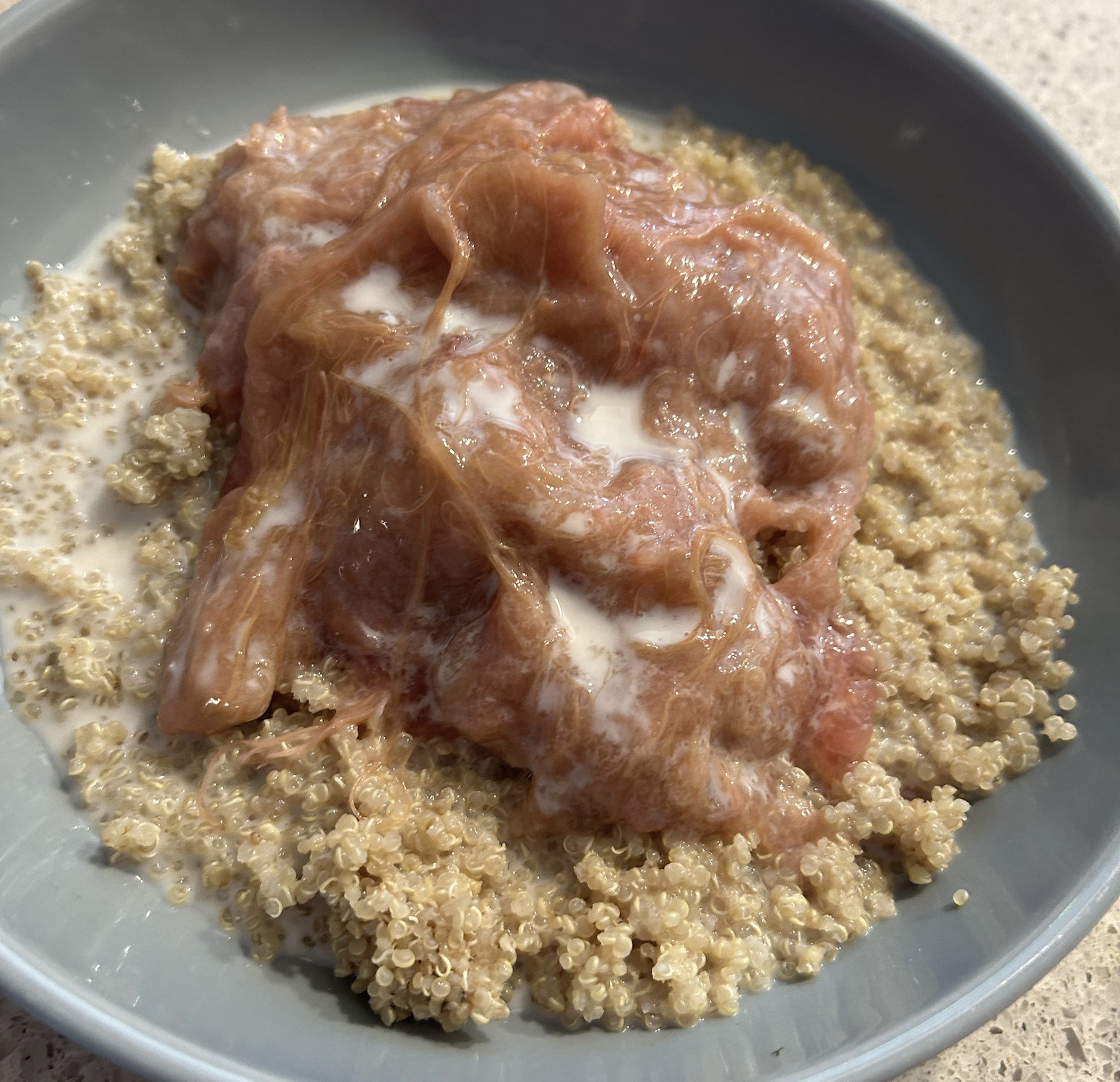 A bowl of cooked quinoa topped with stewed rhubarb and a drizzle of cream.
