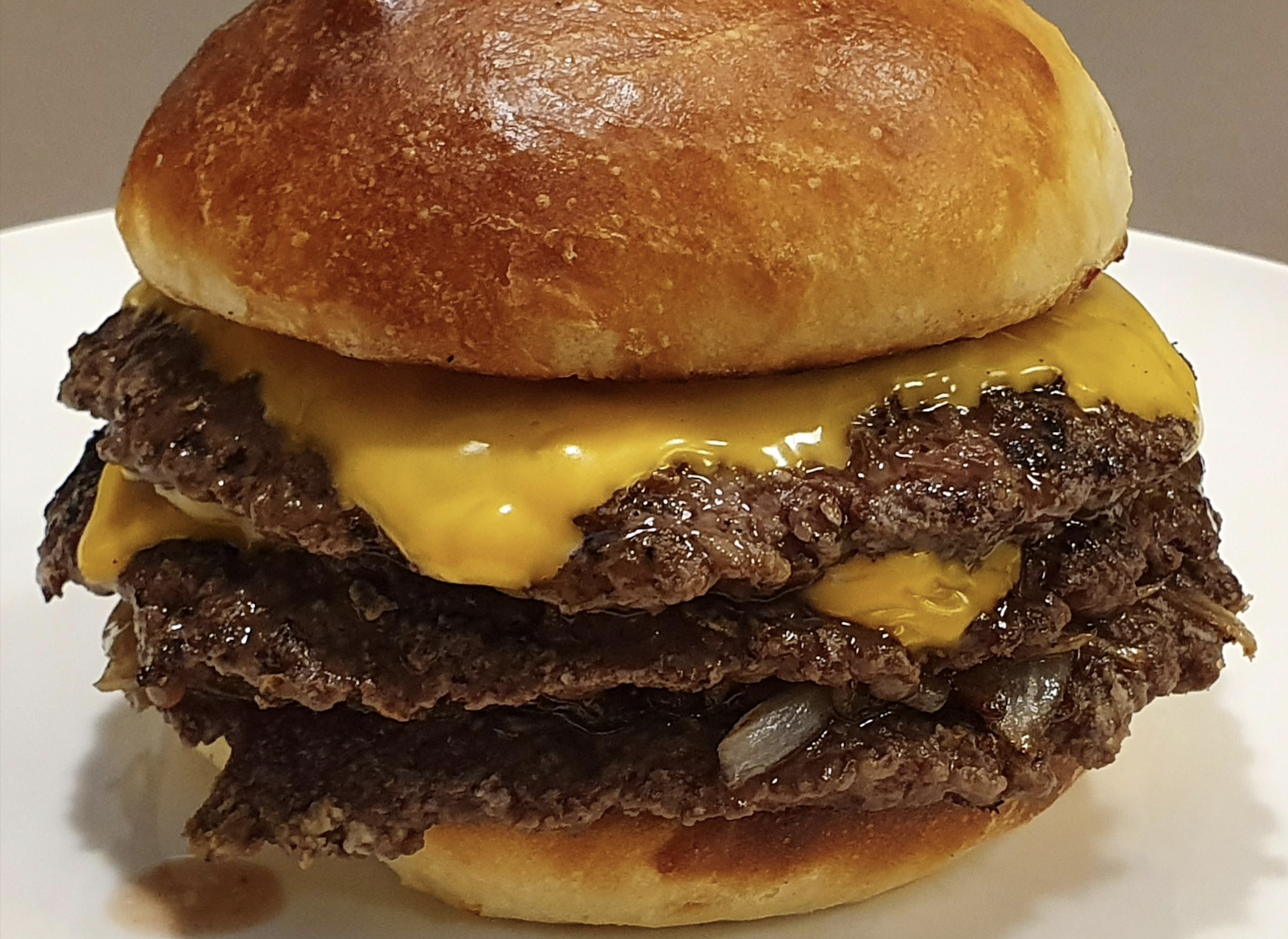 A close-up of a double cheeseburger with two beef patties, melted cheddar cheese, grilled onions, and a shiny toasted bun on a white plate.