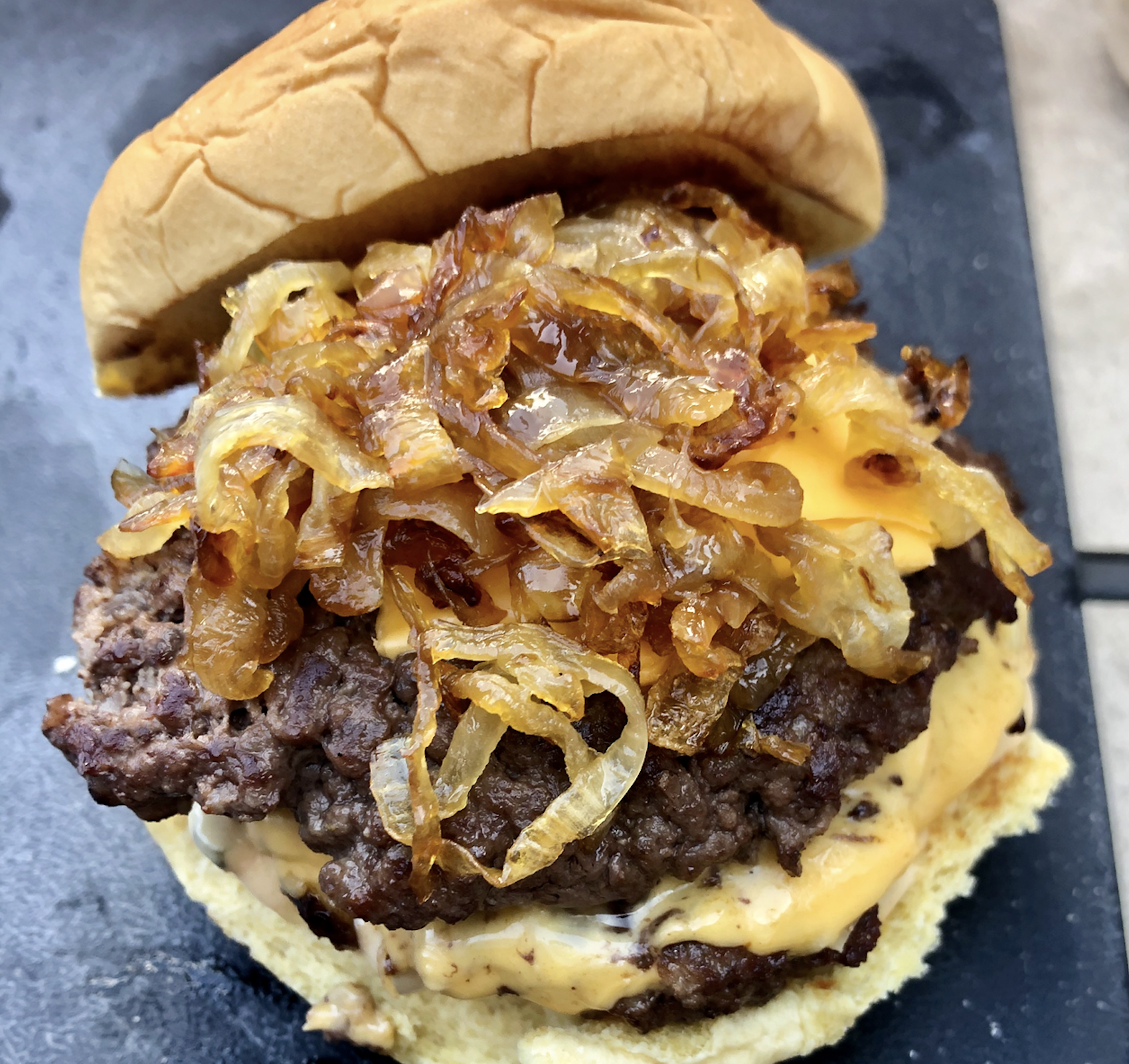 A cheeseburger topped with melted cheese and caramelized onions on a toasted bun, shown close up on a dark surface.