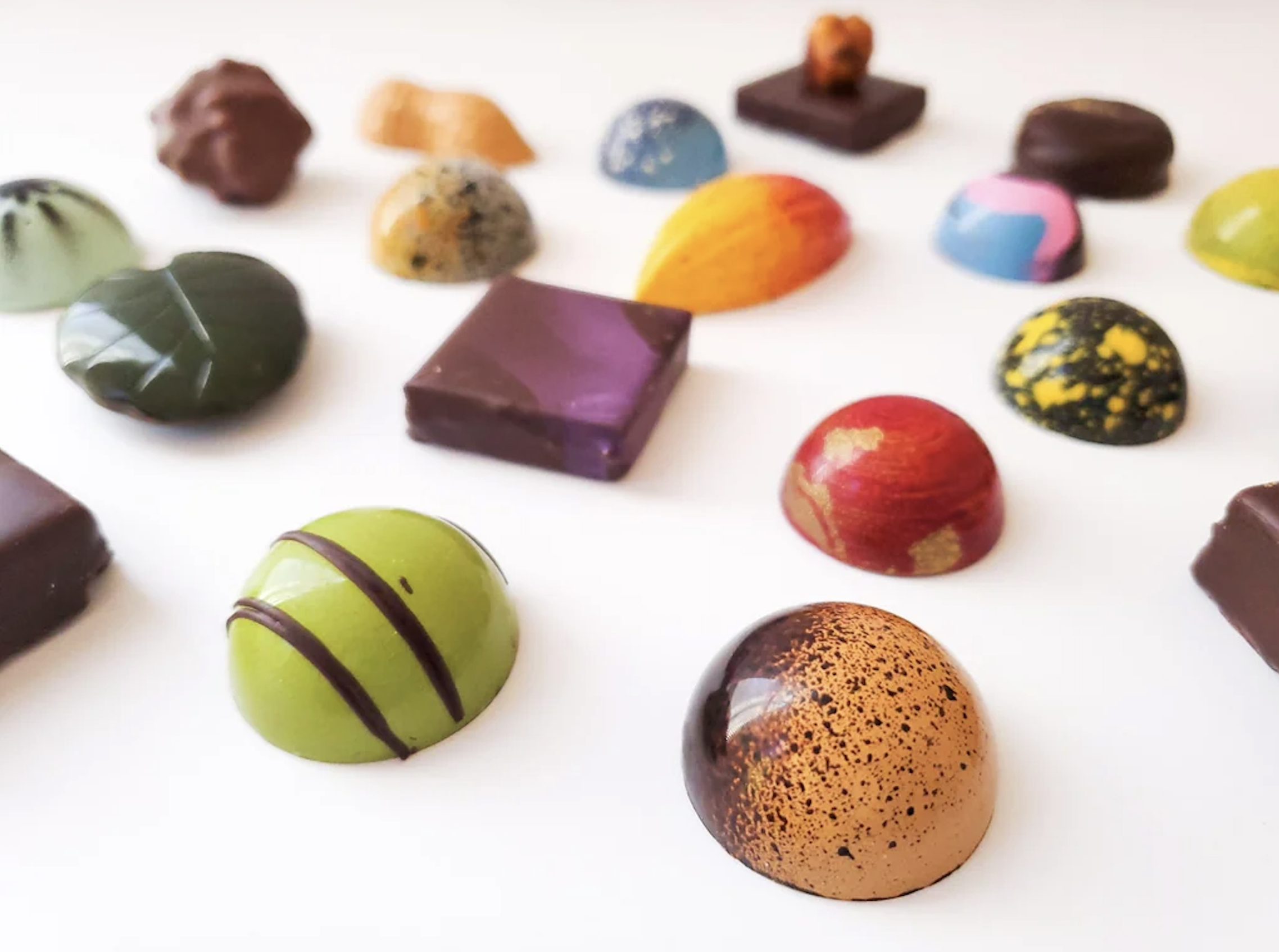 Assorted colorful artisan chocolates in various shapes and designs are arranged on a white surface, creating a vibrant and visually appealing display.