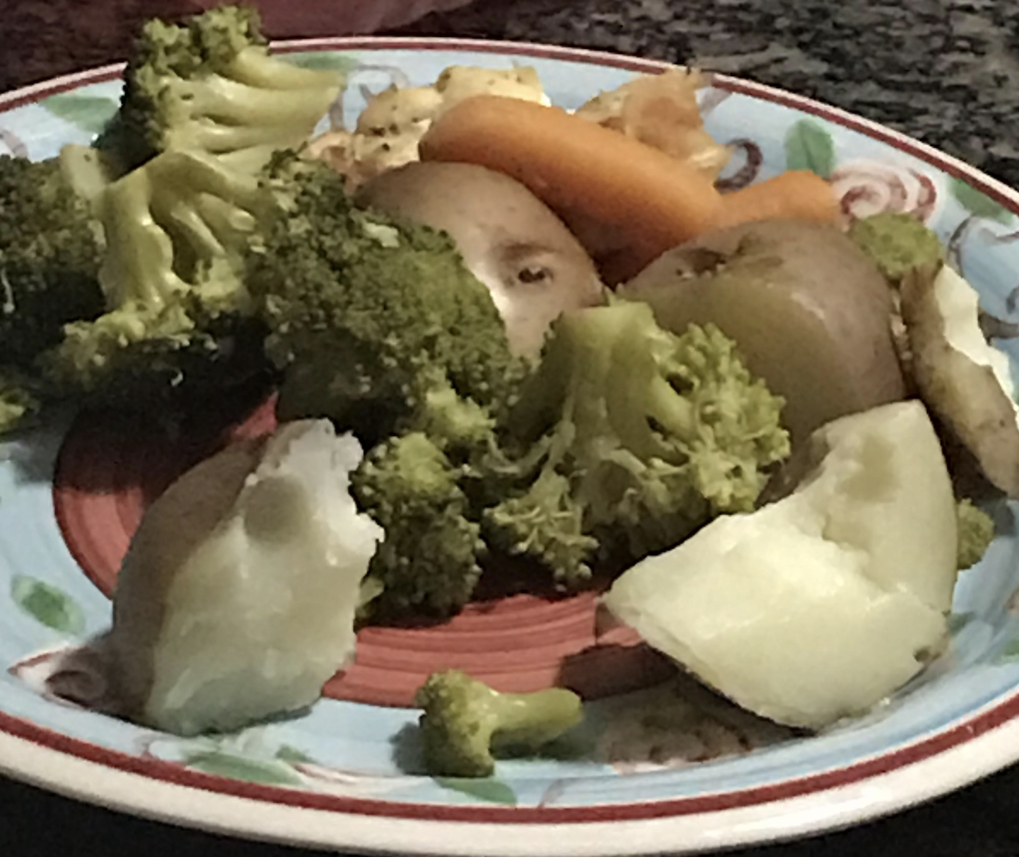 A colorful plate with steamed broccoli, potatoes, carrots, and cauliflower sits on a countertop.