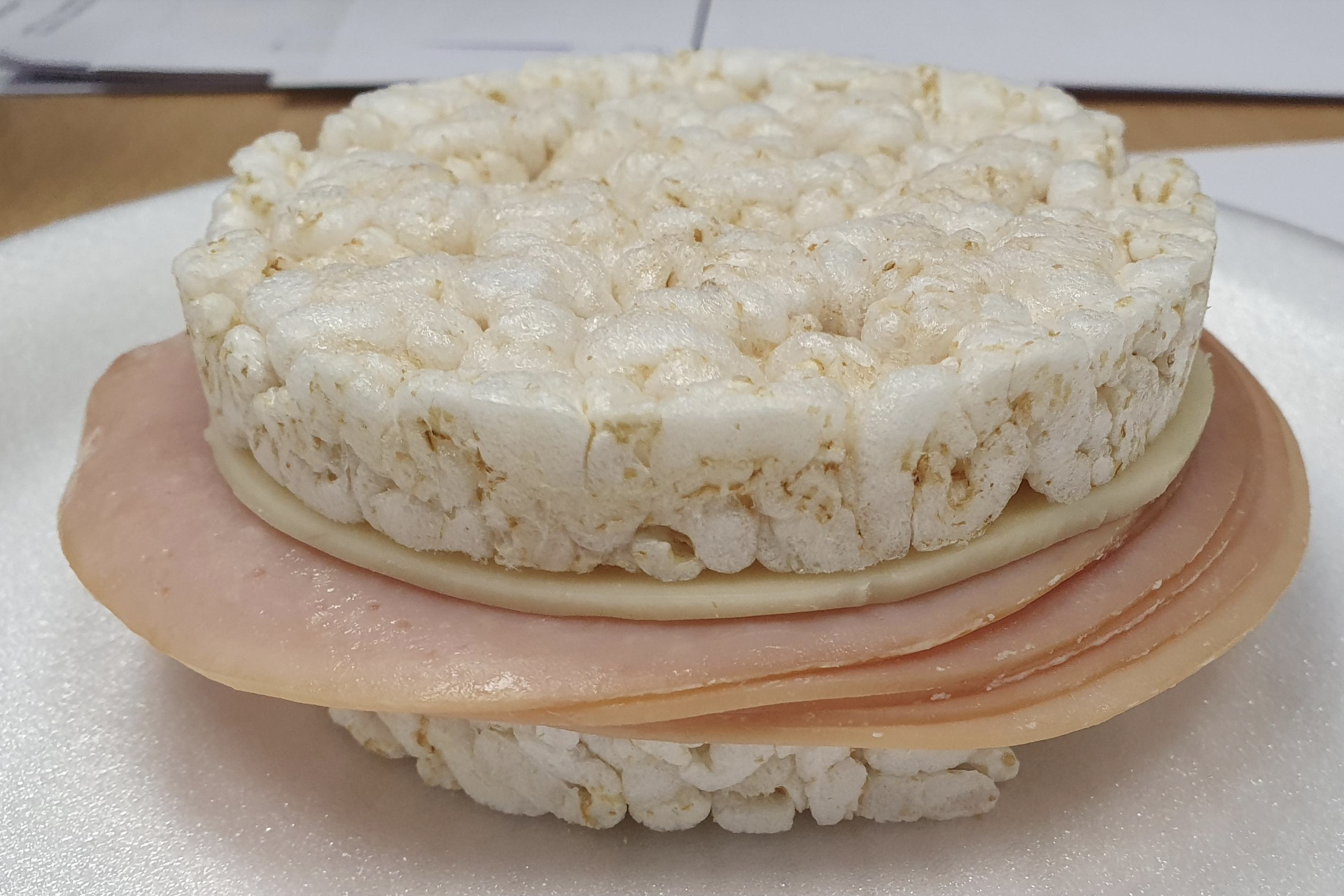A sandwich made with two rice cakes, a slice of cheese, and a slice of deli meat, placed on a white surface.