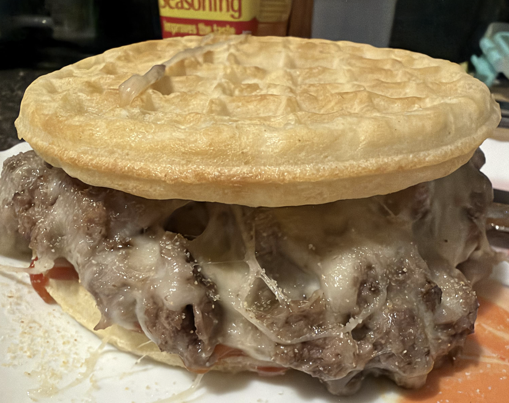 A sandwich made with waffles as the bun, filled with melted cheese, ground beef, and a bit of sauce, on a white plate.