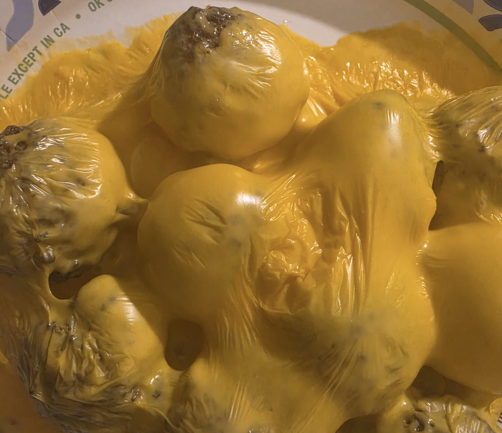 A close-up of several baked potatoes covered in melted yellow cheese, with the cheese forming glossy, uneven mounds over the potatoes.