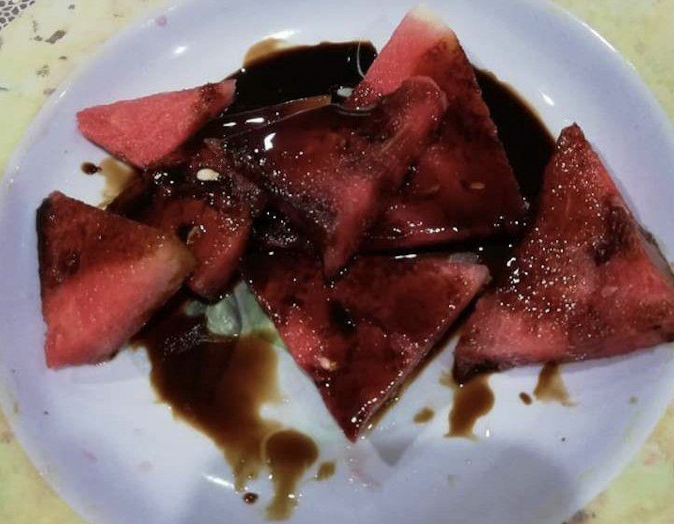 Slices of watermelon topped with dark brown syrup or sauce served on a white plate.