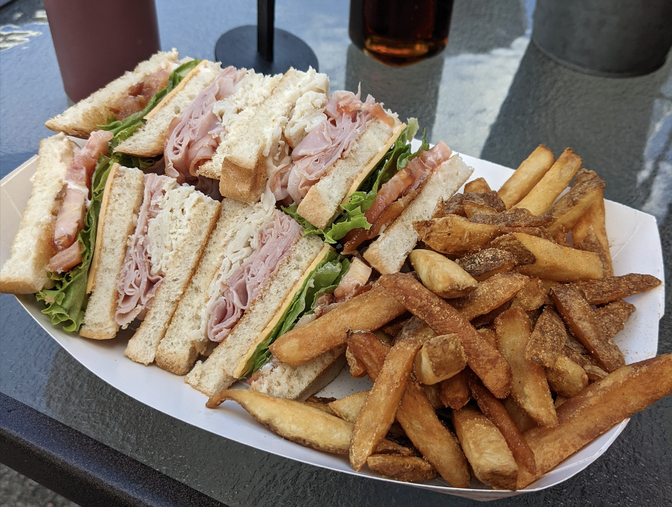 A plate with club sandwiches filled with turkey, ham, lettuce, tomato, and mayo, served with crispy French fries on a table.