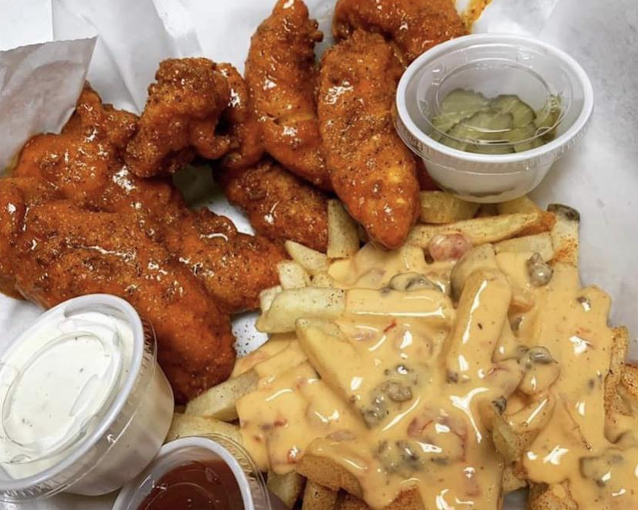 Spicy fried chicken tenders with pickles, crinkle-cut fries topped with creamy sauce and diced veggies, served with ranch and ketchup dipping sauces.