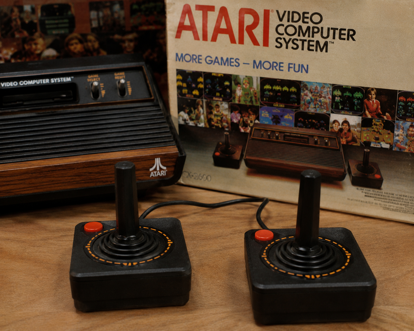 Two Atari joysticks in front of an Atari Video Computer System console, with the original box in the background displaying games and the slogan “More Games – More Fun.”