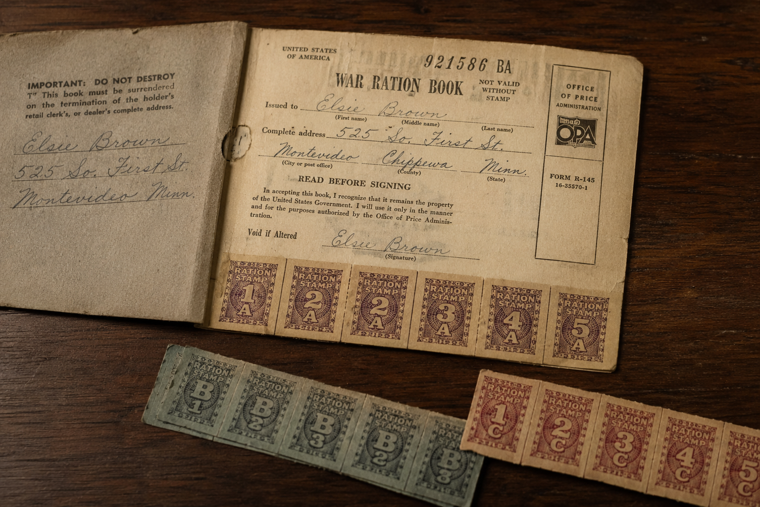 A World War II-era war ration book and ration stamps sit on a wooden surface, showing handwritten details and vintage government-issued food stamps labeled A and B.