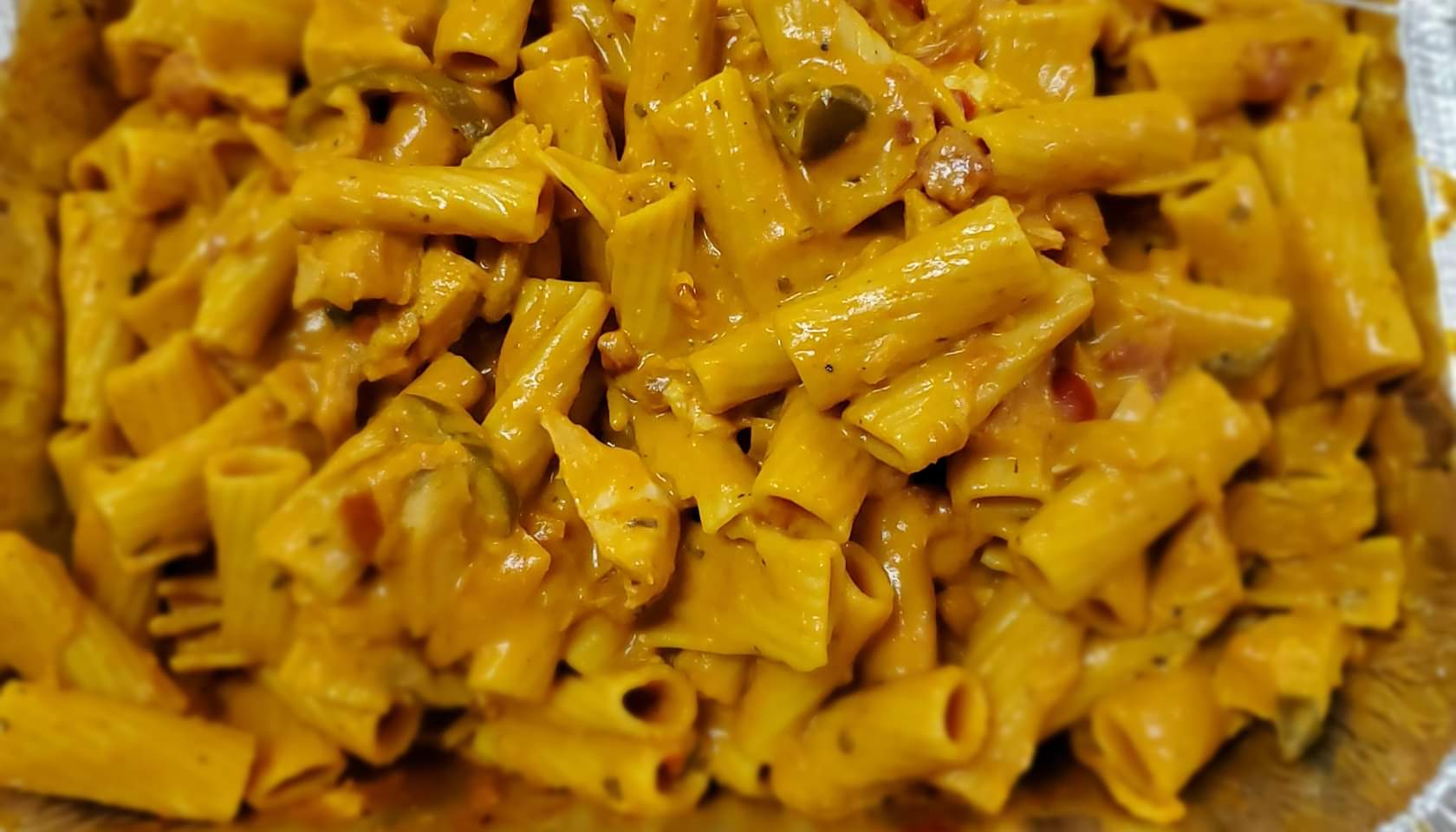 Close-up of creamy rigatoni pasta, one of the restaurant specialties, mixed with a rich orange sauce, herbs, and small pieces of vegetables. The pasta appears freshly cooked and coated evenly with the sauce.