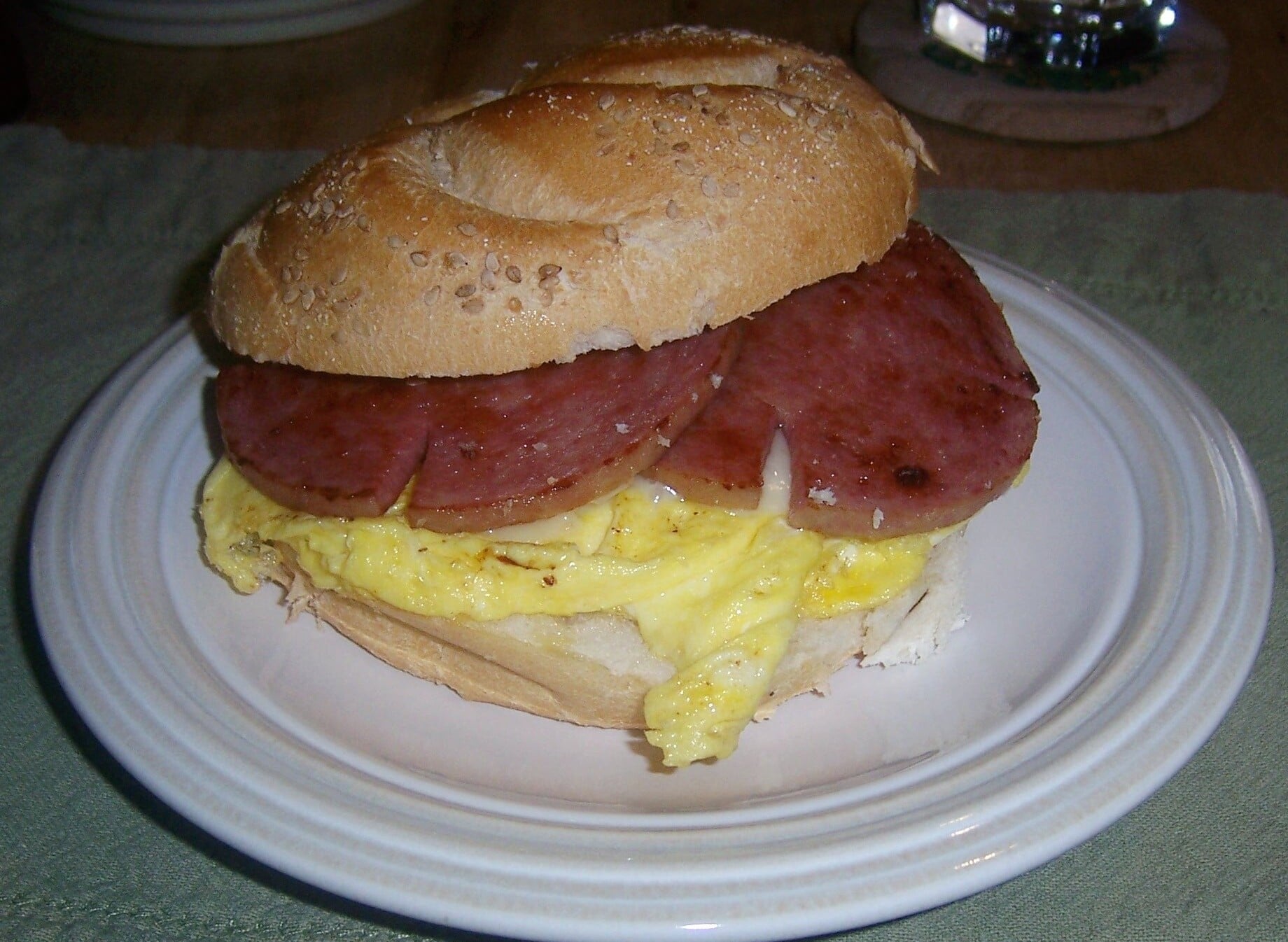 A breakfast sandwich with sliced sausage and a folded omelet, one of our restaurant specialties, is served on a round bagel and placed on a white plate.