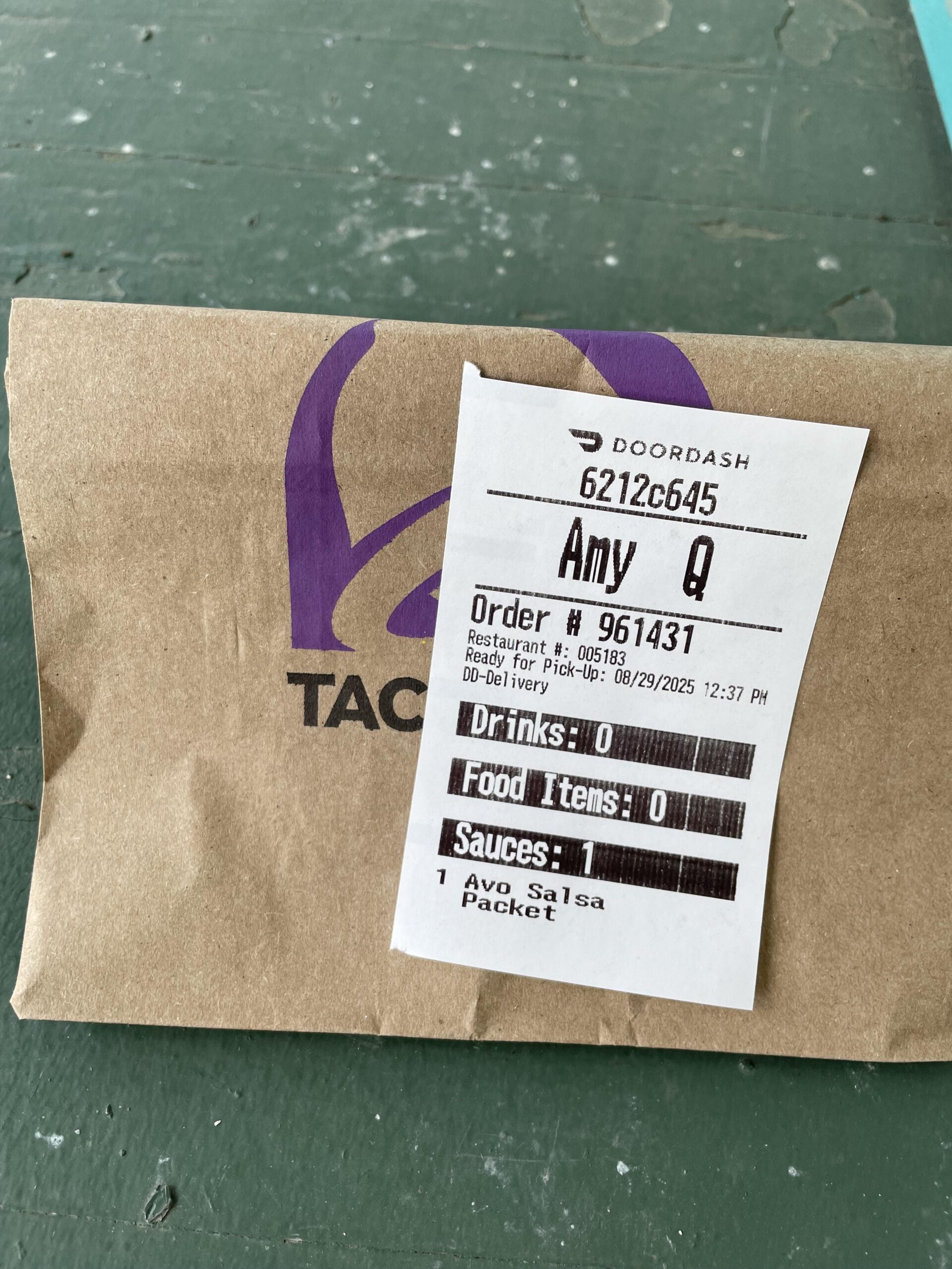 A paper Taco Bell bag with a DoorDash receipt labeled for Amy Q, order #961437, showing 0 drinks, 0 food items, and 1 Avo Salsa packet as the only item.