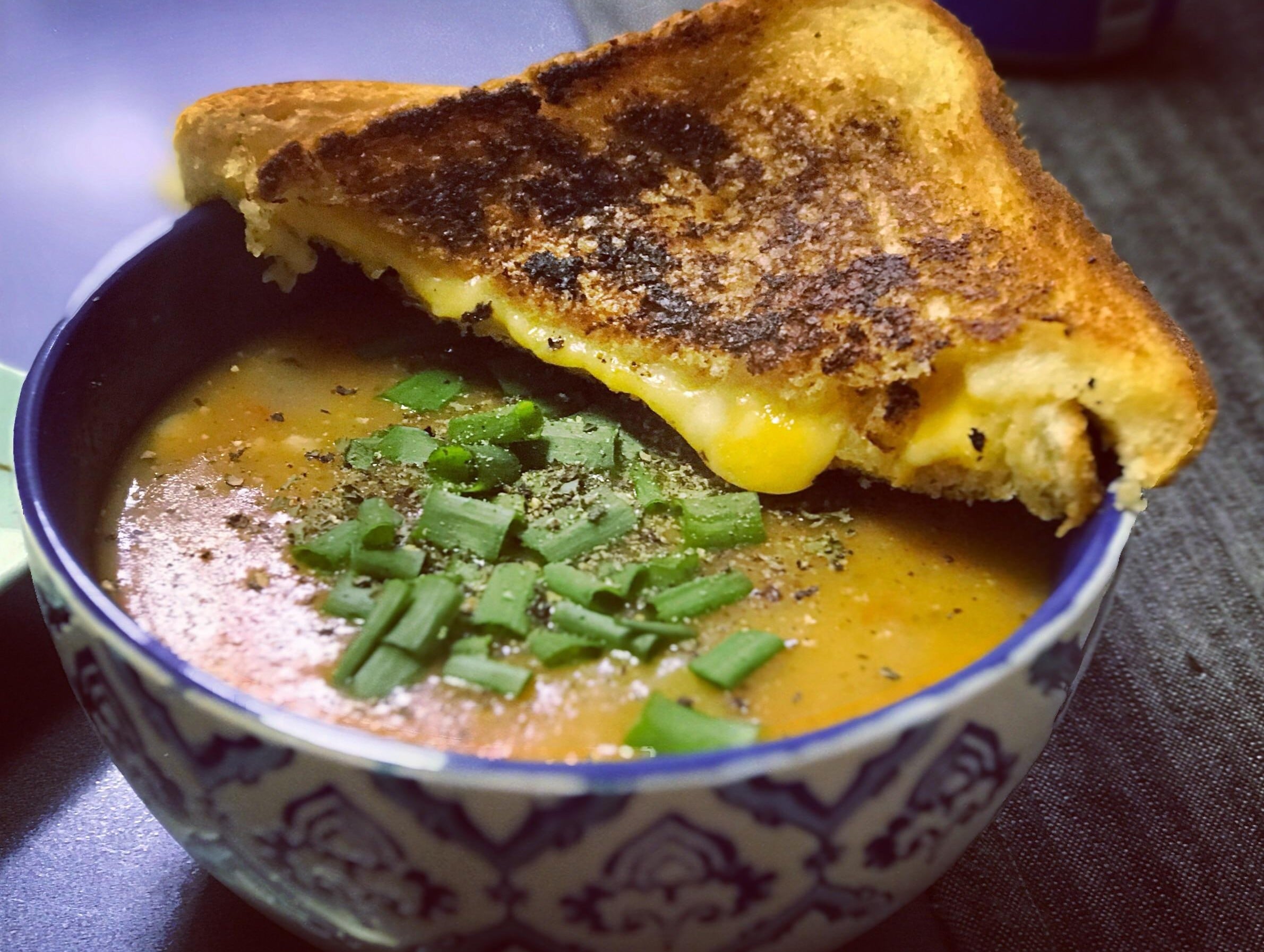 A bowl of soup topped with chopped green onions, served with delicious grilled cheese sandwiches placed on the rim of the bowl.
