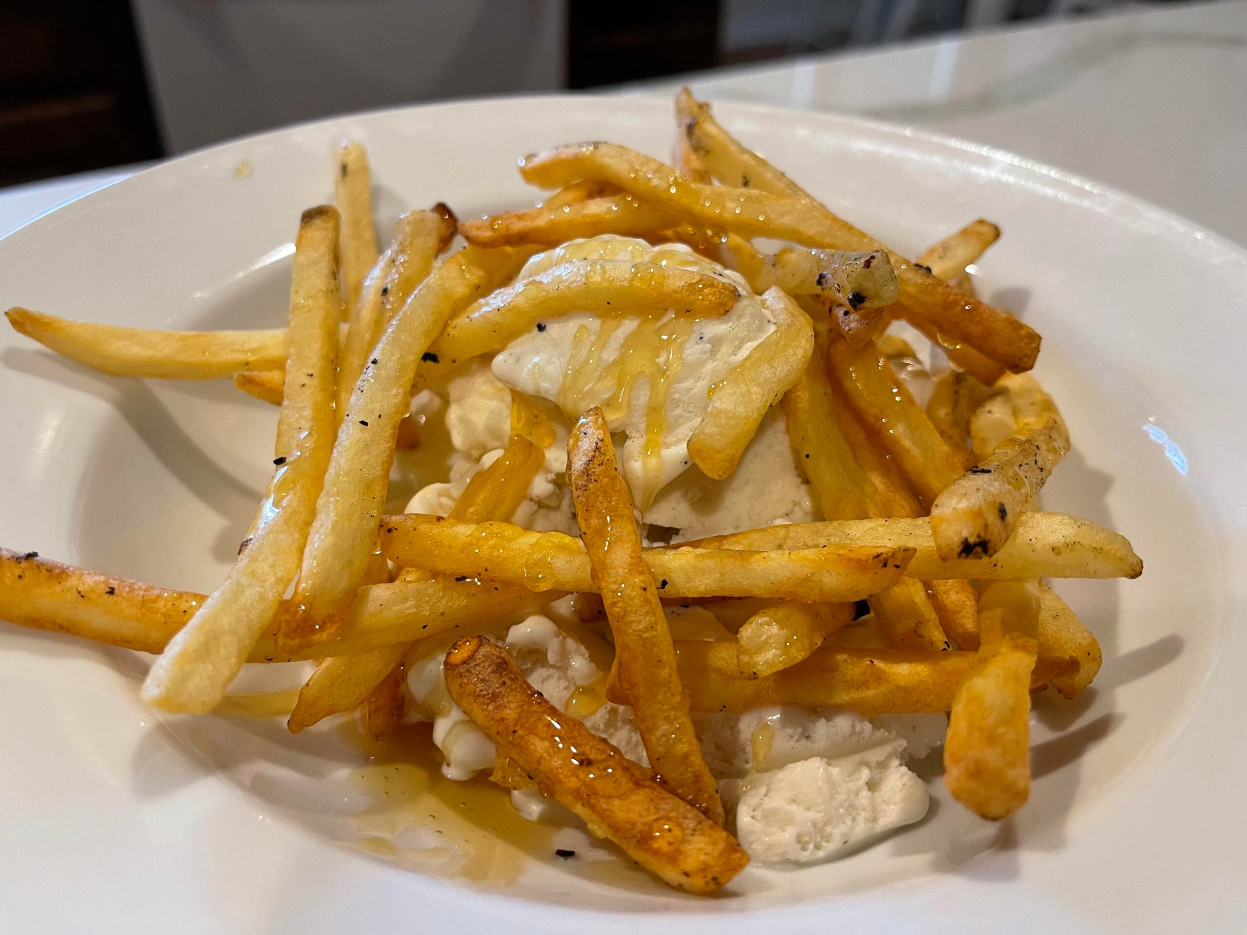 A plate of French fries topped with vanilla ice cream and drizzled with honey, served on a white dish.