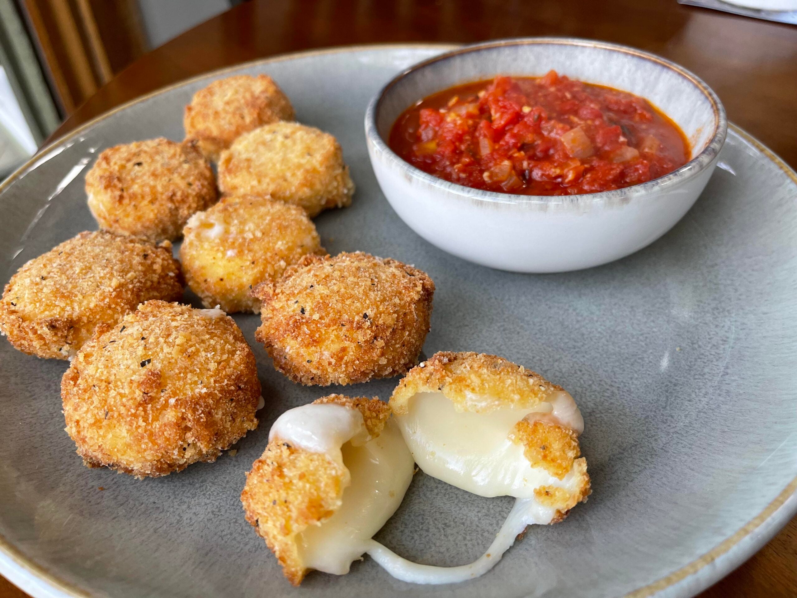 A plate with breaded, fried cheese balls, two split open showing melted cheese inside, served with a bowl of chunky marinara sauce. It's one of the cheese dishes.