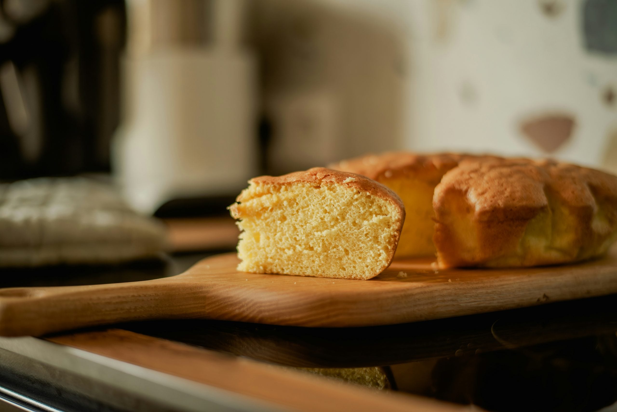 Cornbread, one of the most beloved comfort foods, sits on a wooden cutting board, with the rest of the cake in the background. The scene is set in a kitchen with soft, natural lighting.