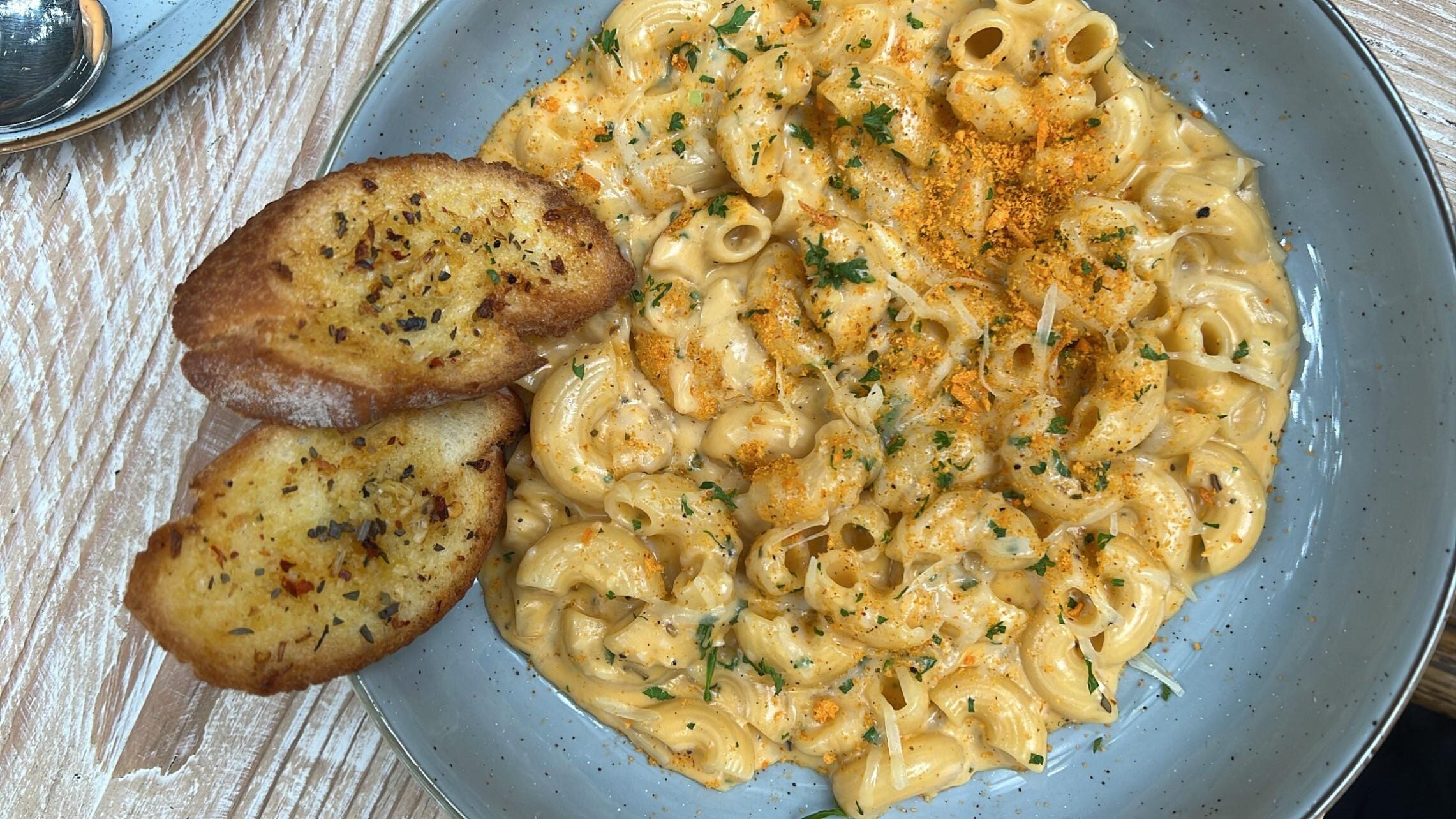 A plate of creamy macaroni and cheese topped with herbs and seasoning, served with two slices of toasted garlic bread on the side—perfect for anyone who loves comfort food and enjoys browsing photos of pasta.